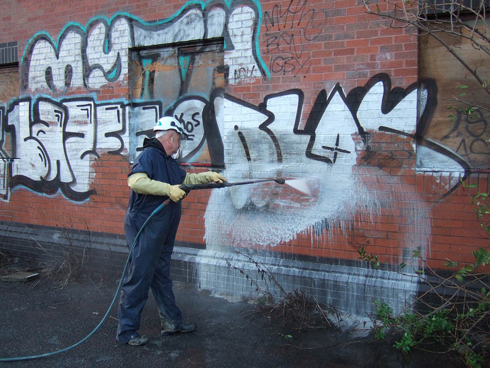 pressure washing professional removing graffiti from brick wall