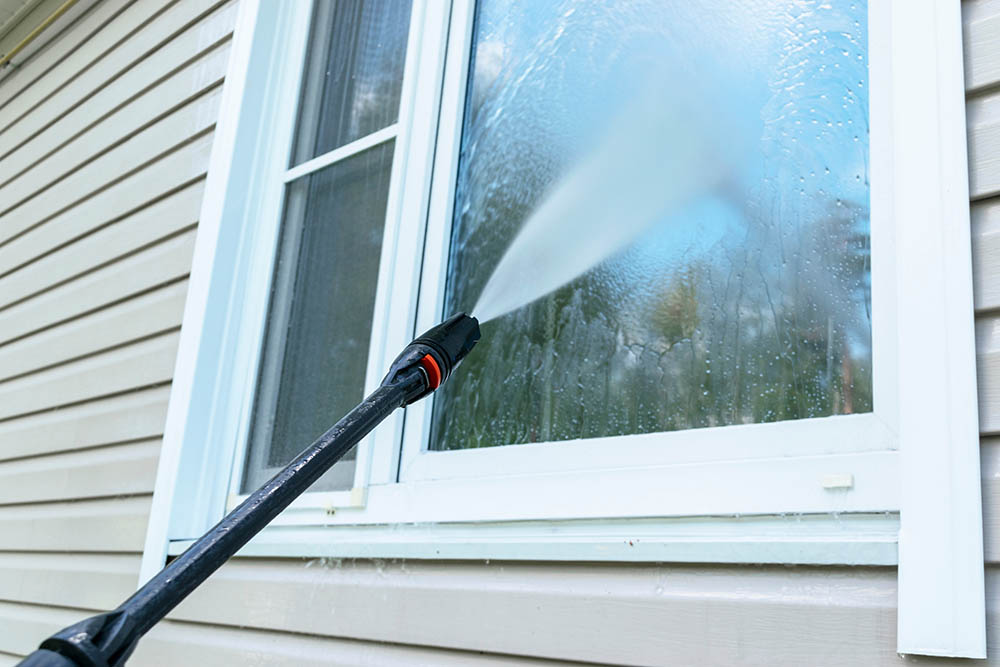 cleaning professional using water cleaning equipment on house window