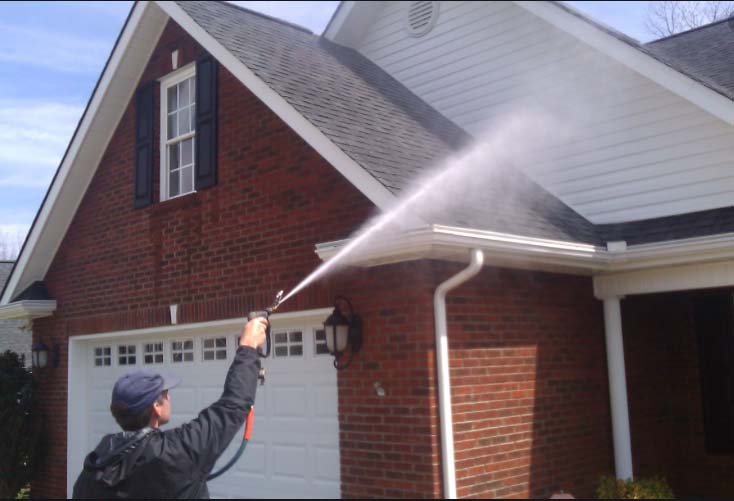 professional house cleaner spraying siding of brick home