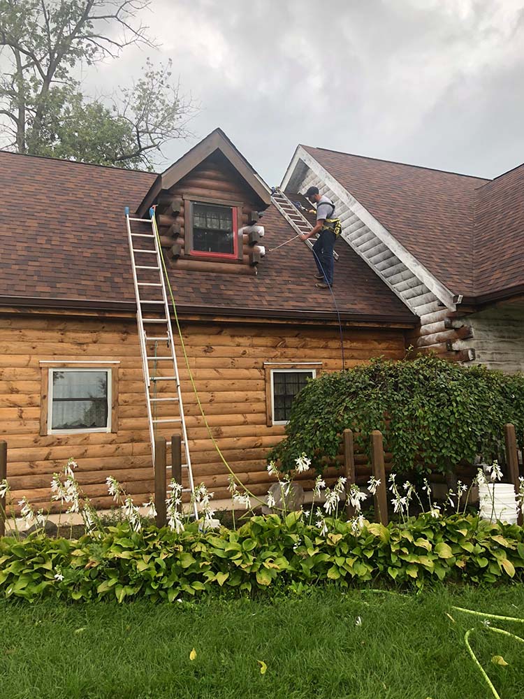 staining professional on roof of log home