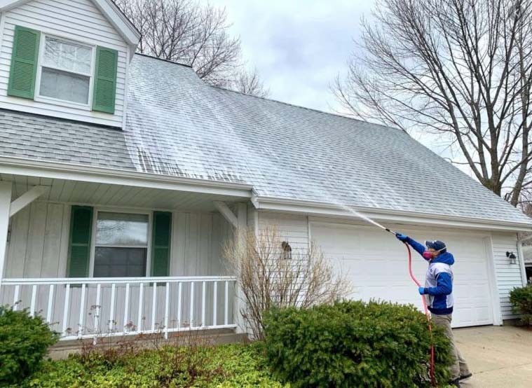 pressure washing professional spraying roof of white home